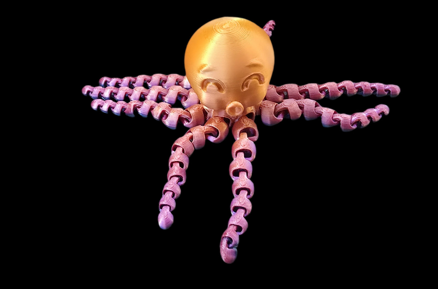 Toy octopus with gold head and pink tentacles on a black background