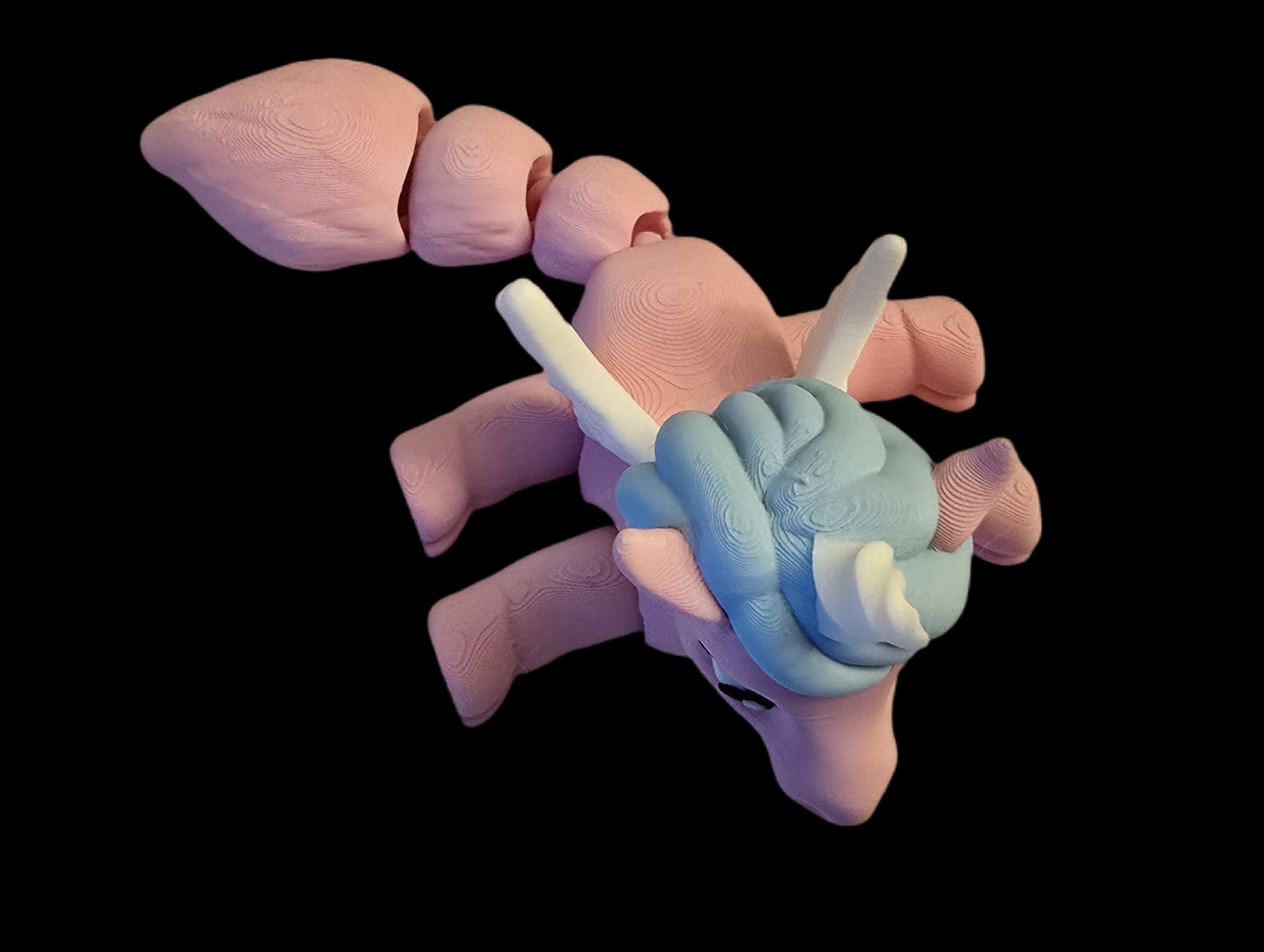 Pink and blue creature figurine on a black background