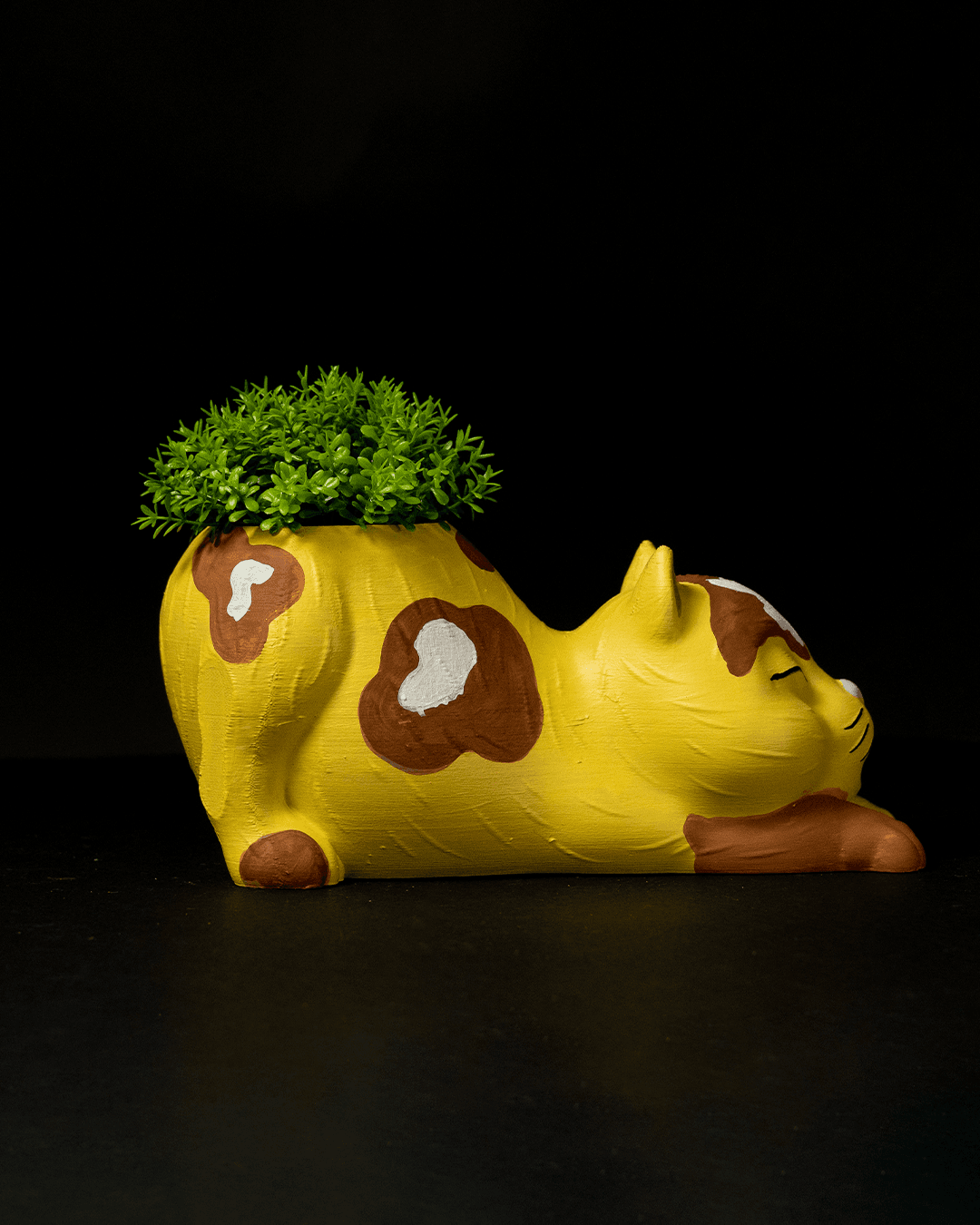 Yellow cow-shaped planter with green plant on a black background